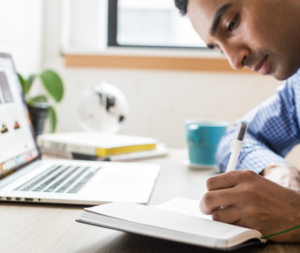 A person studying with a laptop, notebook, and cup of coffee